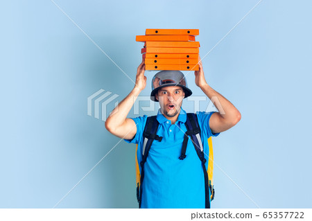 Contacless delivery service during quarantine. Man delivers food and shopping bags during insulation. Emotions of deliveryman isolated on blue background. Contacless delivery service during quarantine. Man delivers food and shopping bags during insulation. Emotions of deliveryman isolated on blue background. 65357722