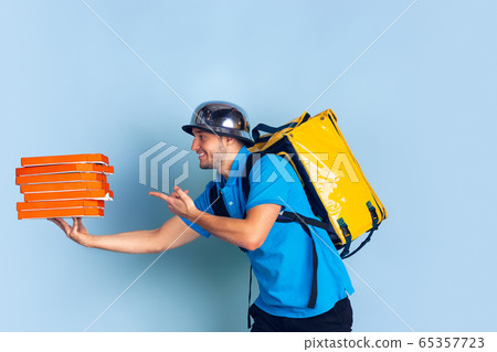 Contacless delivery service during quarantine. Man delivers food and shopping bags during insulation. Emotions of deliveryman isolated on blue background. Contacless delivery service during quarantine. Man delivers food and shopping bags during insulation. Emotions of deliveryman isolated on blue background. 65357723