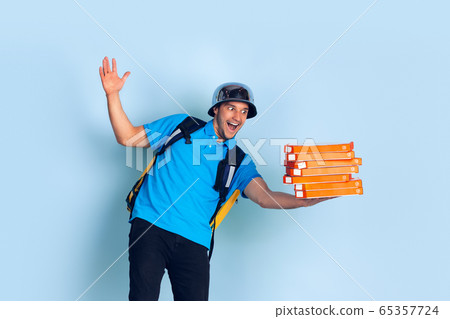 Contacless delivery service during quarantine. Man delivers food and shopping bags during insulation. Emotions of deliveryman isolated on blue background. 65357724