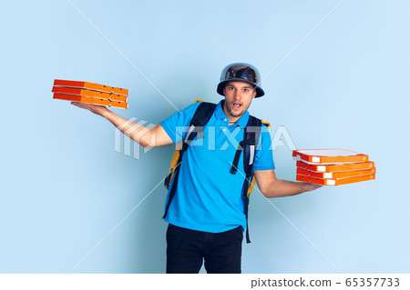 Contacless delivery service during quarantine. Man delivers food and shopping bags during insulation. Emotions of deliveryman isolated on blue background. Contacless delivery service during quarantine. Man delivers food and shopping bags during insulation. Emotions of deliveryman isolated on blue background. 65357733