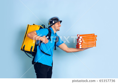 Contacless delivery service during quarantine. Man delivers food and shopping bags during insulation. Emotions of deliveryman isolated on blue background. Contacless delivery service during quarantine. Man delivers food and shopping bags during insulation. Emotions of deliveryman isolated on blue background. 65357736