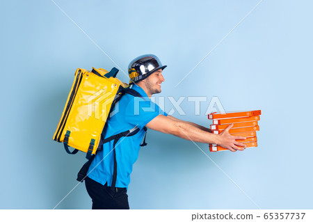 Contacless delivery service during quarantine. Man delivers food and shopping bags during insulation. Emotions of deliveryman isolated on blue background. Contacless delivery service during quarantine. Man delivers food and shopping bags during insulation. Emotions of deliveryman isolated on blue background. 65357737