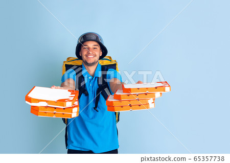 Contacless delivery service during quarantine. Man delivers food and shopping bags during insulation. Emotions of deliveryman isolated on blue background. Contacless delivery service during quarantine. Man delivers food and shopping bags during insulation. Emotions of deliveryman isolated on blue background. 65357738