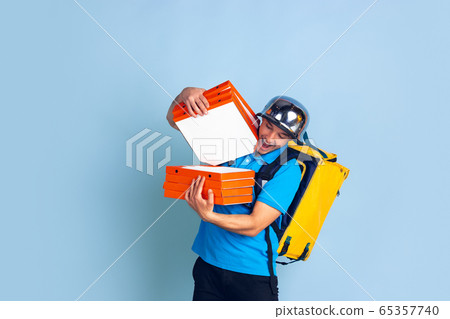 Contacless delivery service during quarantine. Man delivers food and shopping bags during insulation. Emotions of deliveryman isolated on blue background. Contacless delivery service during quarantine. Man delivers food and shopping bags during insulation. Emotions of deliveryman isolated on blue background. 65357740