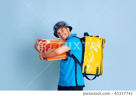 Contacless delivery service during quarantine. Man delivers food and shopping bags during insulation. Emotions of deliveryman isolated on blue background. Contacless delivery service during quarantine. Man delivers food and shopping bags during insulation. Emotions of deliveryman isolated on blue background. 65357742