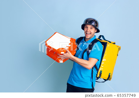 Contacless delivery service during quarantine. Man delivers food and shopping bags during insulation. Emotions of deliveryman isolated on blue background. Contacless delivery service during quarantine. Man delivers food and shopping bags during insulation. Emotions of deliveryman isolated on blue background. 65357749