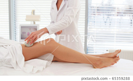 beautician performs a Rf lifting procedure on women's legs in a beauty salon 65359288