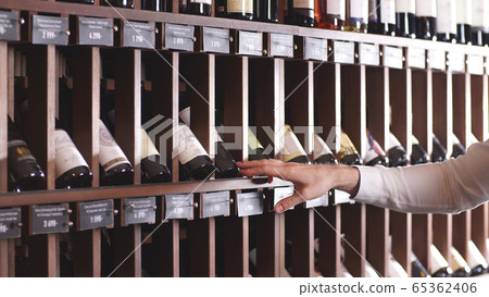 Close-up of a man's hand selecting a bottle of wine from a shelf in a store Close-up of a man's hand selecting a bottle of wine from a shelf in a store 65362406