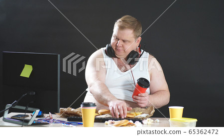 fat programmer works at home remotely at a computer, a person works and eats at the same time, isolated black background fat programmer works at home remotely at a computer, a person works and eats at the same time, isolated black background 65362472