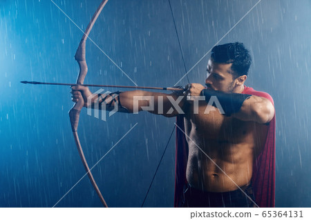 Muscular wet spartan shooting from bow. 65364131