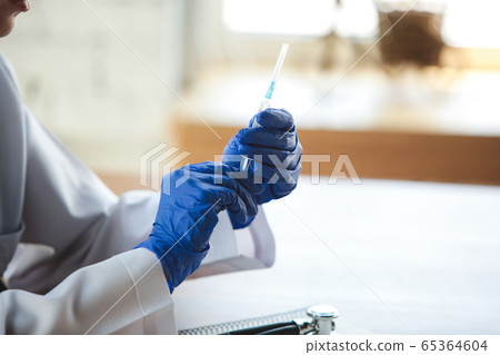 Close up of doctors hands wearing blue protective gloves with stethoscope and syringe on wooden table background 65364604