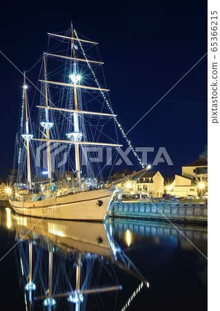Sailing boat anchored amd moored in old town of Klaipeda, Lithuania, with evening lights on. Medieval town and barquentine reflection in calm waters. 65366215