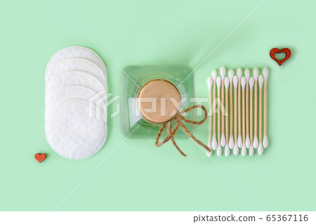 Cleansing lotion or tonic in a glass jar, cotton pads and cotton buds wood stick on a pastel mint Cleansing lotion or tonic in a glass jar, cotton pads and cotton buds wood stick on a pastel mint 65367116
