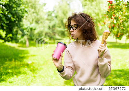 attractive student with a cup of coffee and ice cream walking in the park during the lunch break attractive student with a cup of coffee and ice cream walking in the park during the lunch break 65367272