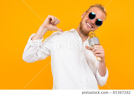 portrait of a blond man in a white shirt singing into a microphone on a yellow background. 65367282