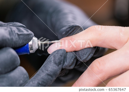Process manicure close-up. Preparation for hardware manicure. Beautician in rubber gloves cuts the cuticle and processes nails. Process manicure close-up. Preparation for hardware manicure. Beautician in rubber gloves cuts the cuticle and processes nails. 65367647