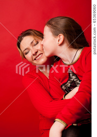 Mom and daughter lovingly cuddle on a red background 65369060