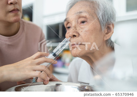 Nasal irrigation,female caregiver is helping senior woman wash her nose,nasal cleaning with syringe and saline,elderly people having sinus allergies,sinusitis,dust allergic,irrigation during influenza 65370946