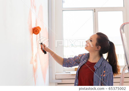 Pretty young woman with painting roller indoors. Redecoration, renovation, apartment repair and refreshment concept. 65375002