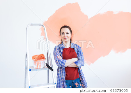 Renovation, redecoration and repair concept - Cheerful woman painting wall in new home. Renovation, redecoration and repair concept - Cheerful woman painting wall in new home. 65375005