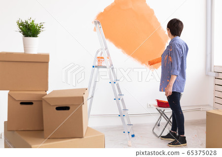 Middle-aged woman painting the walls of new home. Renovation, repair and redecoration concept. Middle-aged woman painting the walls of new home. Renovation, repair and redecoration concept. 65375028