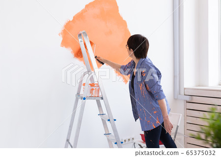 Middle-aged woman painting the walls of new home. Renovation, repair and redecoration concept. Middle-aged woman painting the walls of new home. Renovation, repair and redecoration concept. 65375032