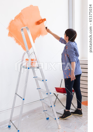 Happy smiling middle-aged woman painting interior wall of new house. Redecoration, renovation, apartment repair and refreshment concept. Happy smiling middle-aged woman painting interior wall of new house. Redecoration, renovation, apartment repair and refreshment concept. 65375034
