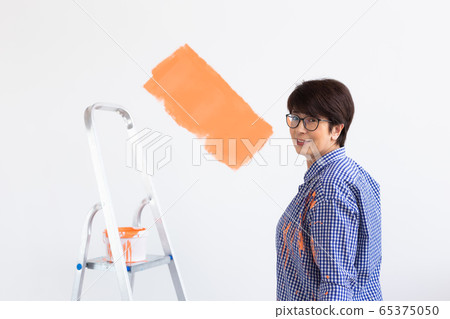 Lovely middle-aged woman painting wall. Renovation, redecoration and repair concept. Lovely middle-aged woman painting wall. Renovation, redecoration and repair concept. 65375050