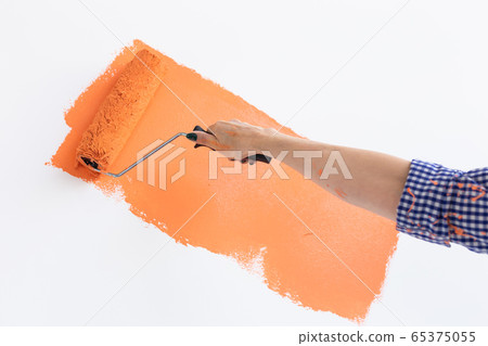Close-up hand painting interior wall with paint roller in new house. A woman with roller applying paint on a wall. 65375055