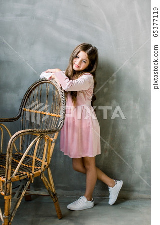 Cute baby girl 5-6 year old wearing stylish pink dress overgrey background. Looking at camera. Birthday party. Celebration. Cute baby girl 5-6 year old wearing stylish pink dress overgrey background. Looking at camera. Birthday party. Celebration. 65377119