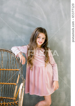 Cute baby girl 5-6 year old wearing stylish pink dress overgrey background. Looking at camera. Birthday party. Celebration. Cute baby girl 5-6 year old wearing stylish pink dress overgrey background. Looking at camera. Birthday party. Celebration. 65377120