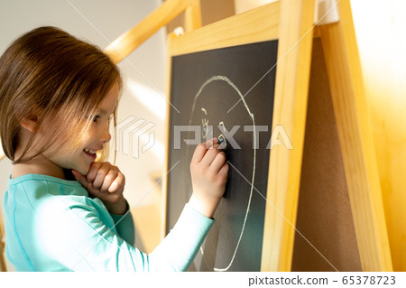 Smiling little girl drawing face on chalkboard 65378723