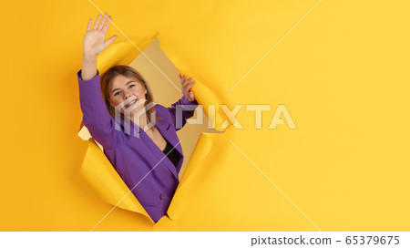 Cheerful young woman poses in torn yellow paper hole background, emotional and expressive, flyer with copyspace Cheerful young woman poses in torn yellow paper hole background, emotional and expressive, flyer with copyspace 65379675