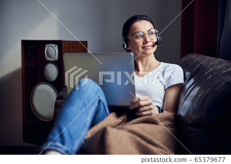 Caucasian pretty girl in headphones sitting on sofa with laptop computer Caucasian pretty girl in headphones sitting on sofa with laptop computer 65379677