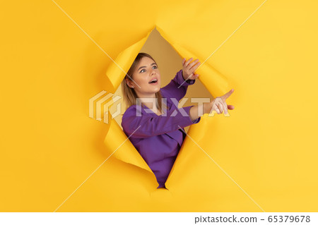 Cheerful young woman poses in torn yellow paper hole background, emotional and expressive Cheerful young woman poses in torn yellow paper hole background, emotional and expressive 65379678