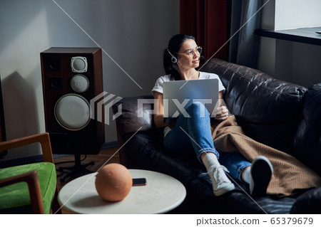 Caucasian calm lady in headphones sitting on sofa in her apartment 65379679