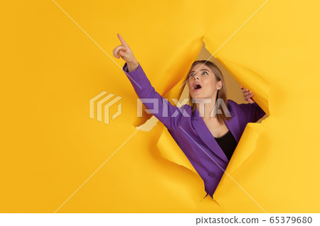 Cheerful young woman poses in torn yellow paper hole background, emotional and expressive Cheerful young woman poses in torn yellow paper hole background, emotional and expressive 65379680