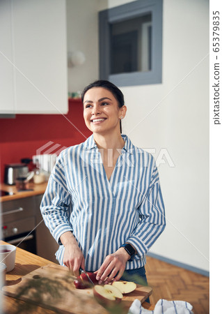Pretty Caucasian lady cutting apple with knife in her kitchen Pretty Caucasian lady cutting apple with knife in her kitchen 65379835