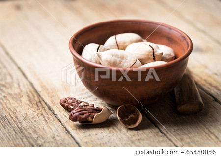 Dried organic Pecan nuts in orange ceramic bowl 65380036