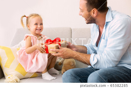 Excited girl holding her present sitting with dad 65382285