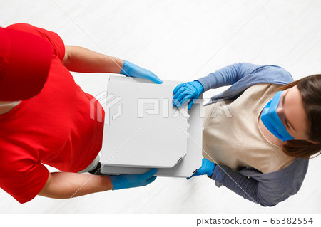 Sterile delivery of pizza. Courier and client in medical masks and gloves Sterile delivery of pizza. Courier and client in medical masks and gloves 65382554