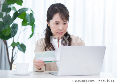 一名中年婦女比較存摺和個人計算機 一名中年婦女比較存摺和個人計算機 65391034