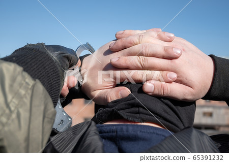 a police officer puts handcuffs on the hands of a bandit 65391232