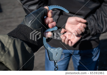 a police officer puts handcuffs on the hands of a bandit 65391961