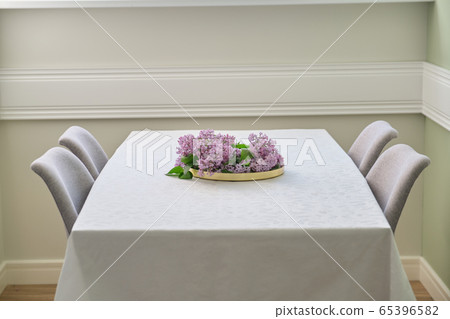 Living room dining area with 4 chairs near window, bouquet of lilac flowers on the table Living room dining area with 4 chairs near window, bouquet of lilac flowers on the table 65396582