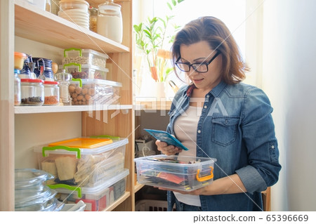 Woman at home in kitchen, near wooden shelves with food Woman at home in kitchen, near wooden shelves with food 65396669