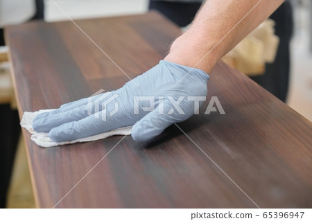 Closeup of workers hand covering wooden plank with finishing protective cover for wood Closeup of workers hand covering wooden plank with finishing protective cover for wood 65396947