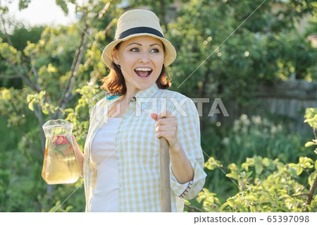 Smiling woman with jug of refreshing natural homemade drink in the summer garden 65397098