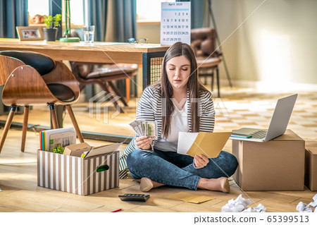 Young woman sitting on the floor and calculating expenses Young woman sitting on the floor and calculating expenses 65399513