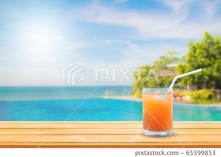 Welcome drink orange juice punch put on wooden table nearly swimming pool with blue water and blue sky in background. Welcome drink orange juice punch put on wooden table nearly swimming pool with blue water and blue sky in background. 65399853